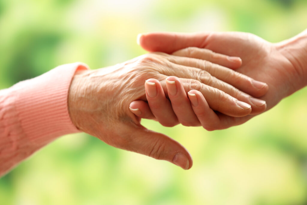 Old and young holding hands on light background, closeup